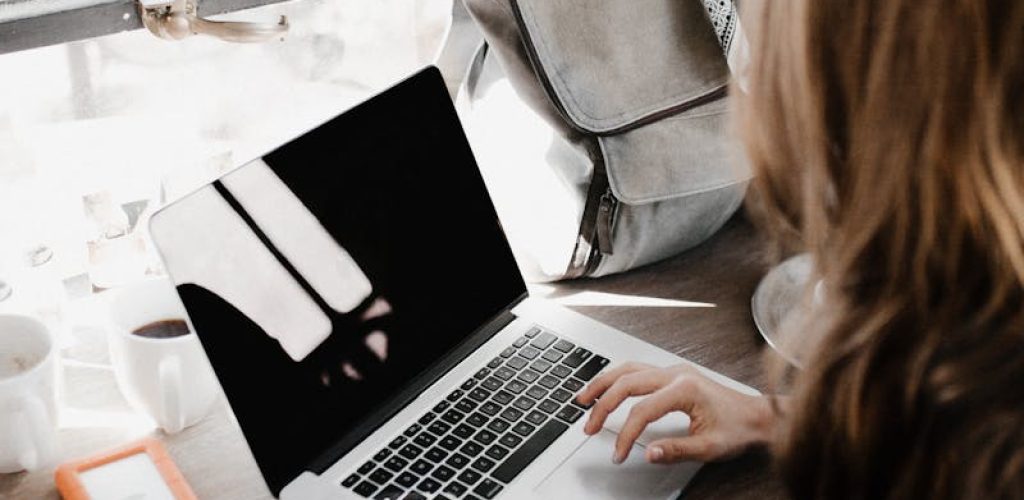 A young woman works remotely at a café, using her laptop and external hard drive.
